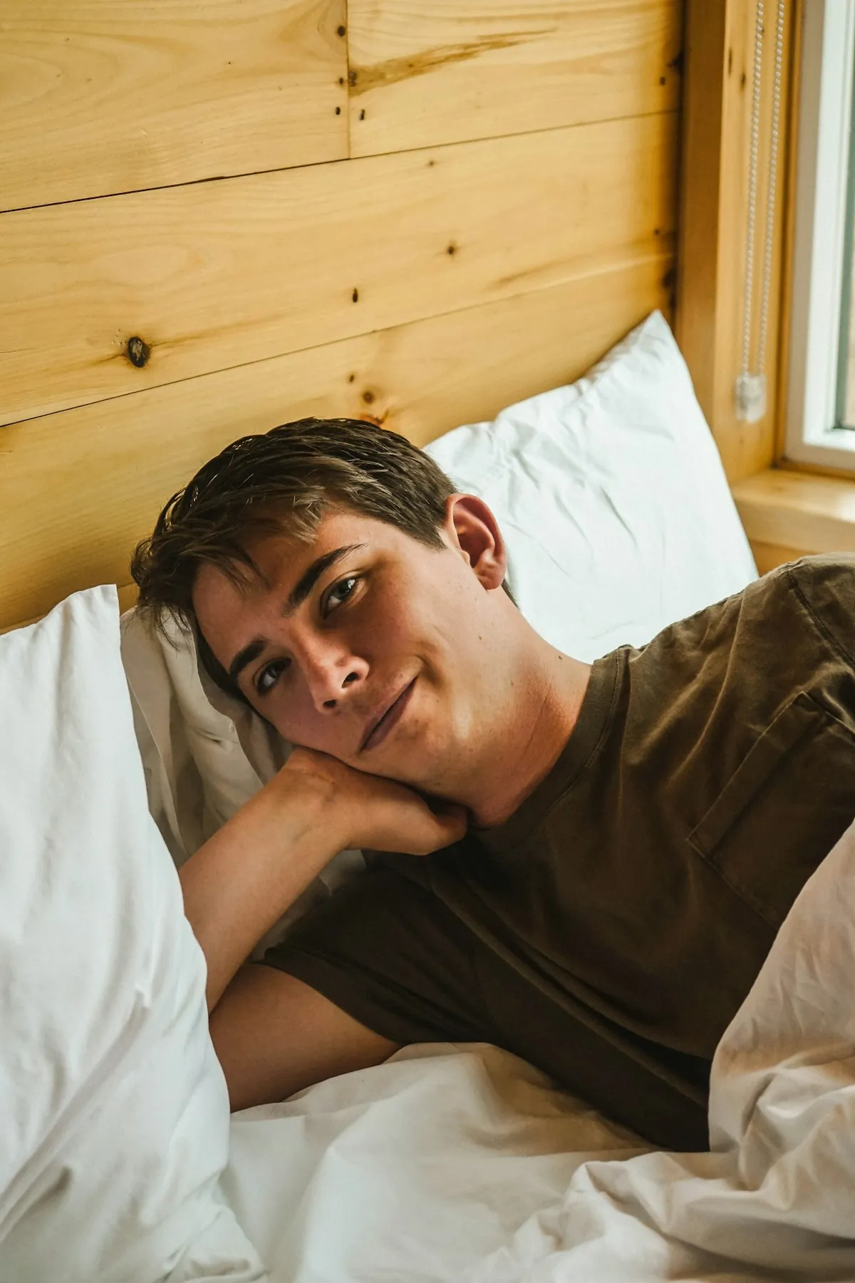 Smiling man lying on his back with his head on a pillow, relaxed on a mattress